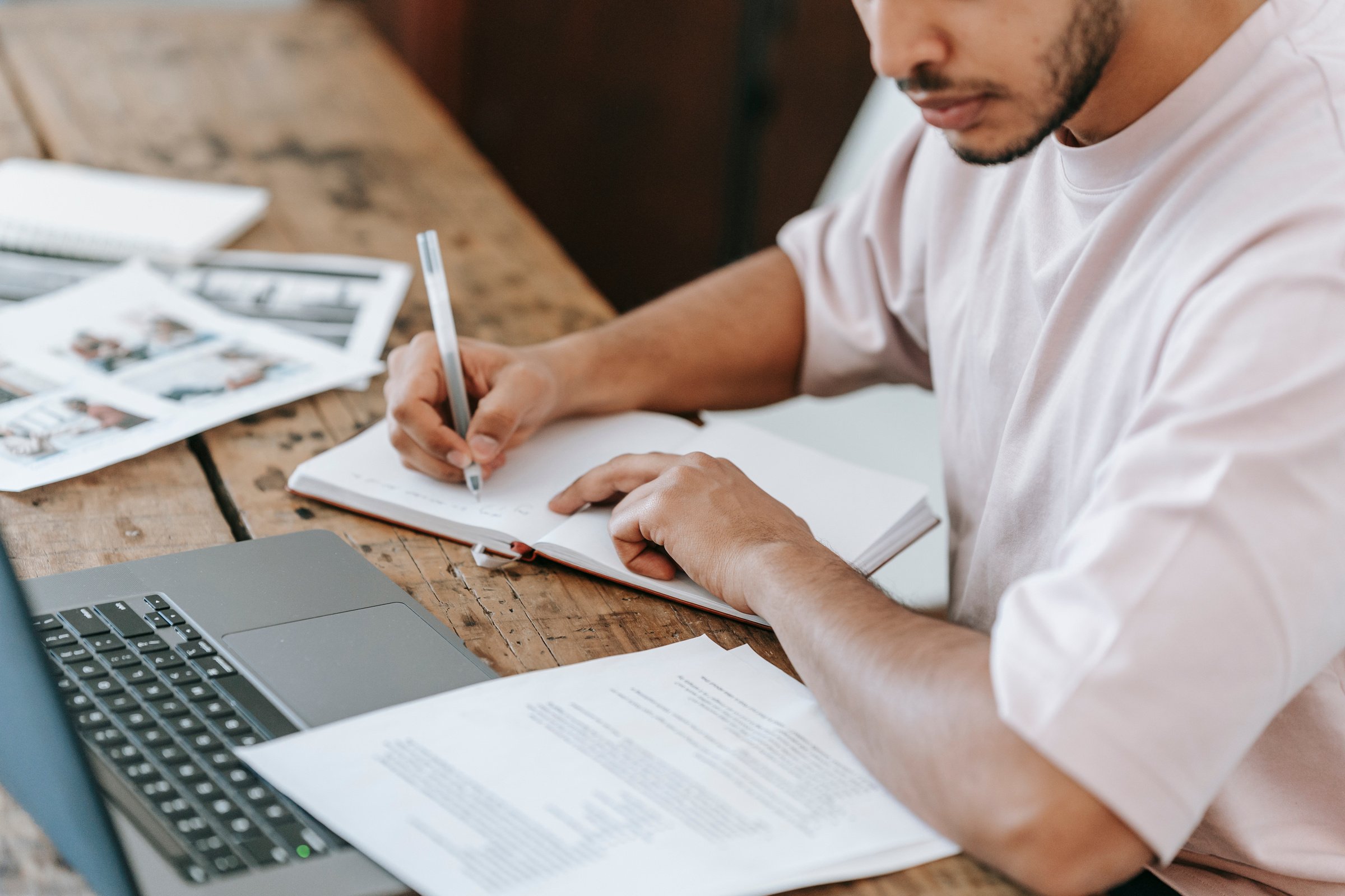 Crop student writing in agenda at desk with laptop